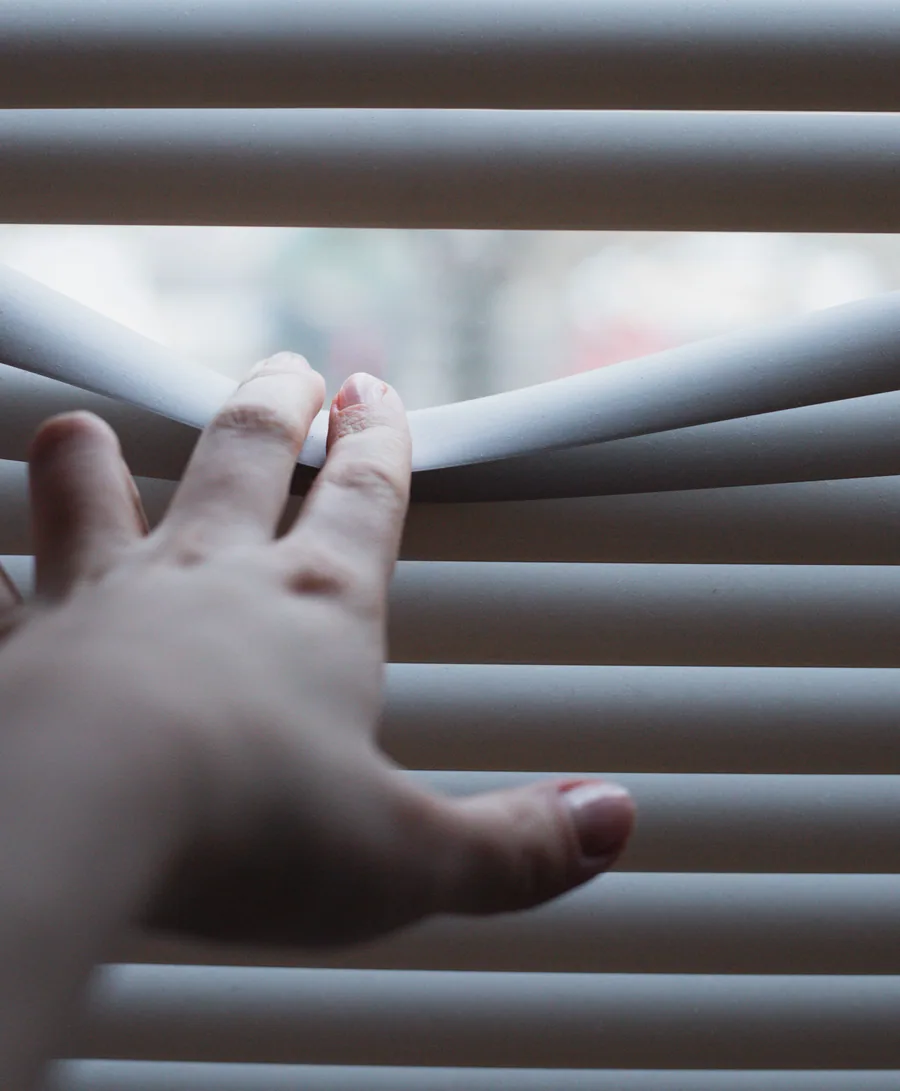 A hand adjusting horizontal blinds to control daylight